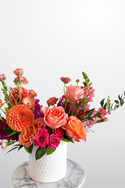 Colorful flower arrangement in a white vase on a marble surface with a light gray background